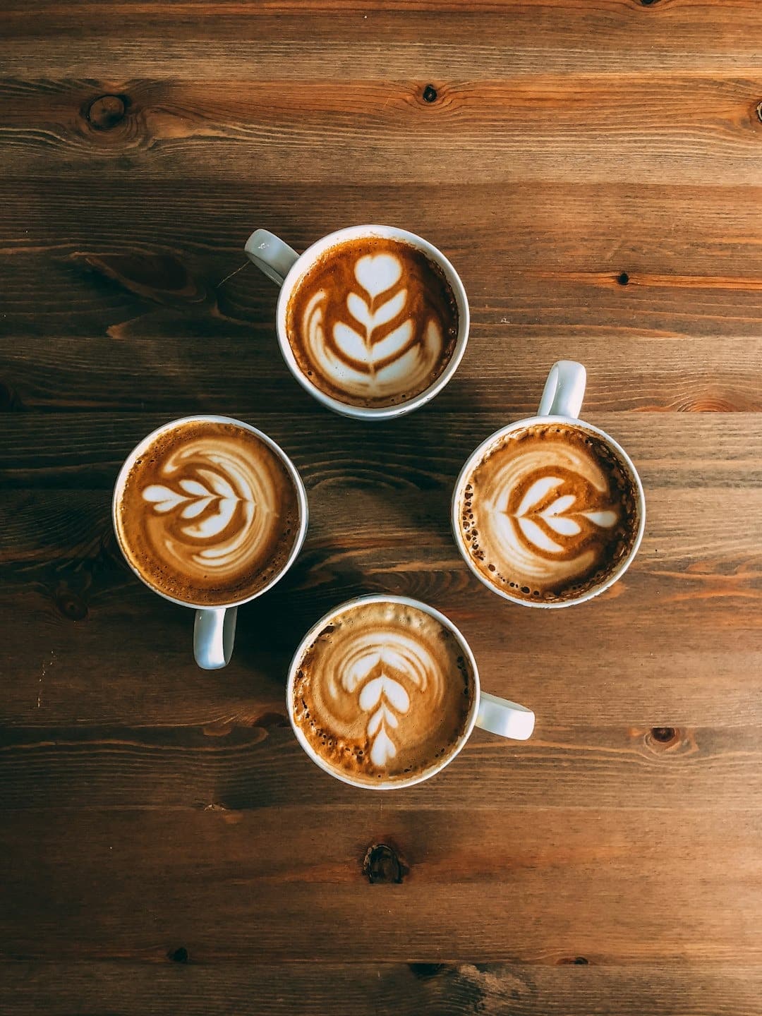Four cups of coffee with latte art on a wooden table.